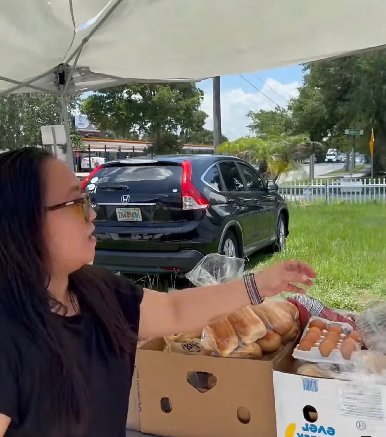 A volunteer reaching over boxes of packaged bread and hot dogs under a canopy