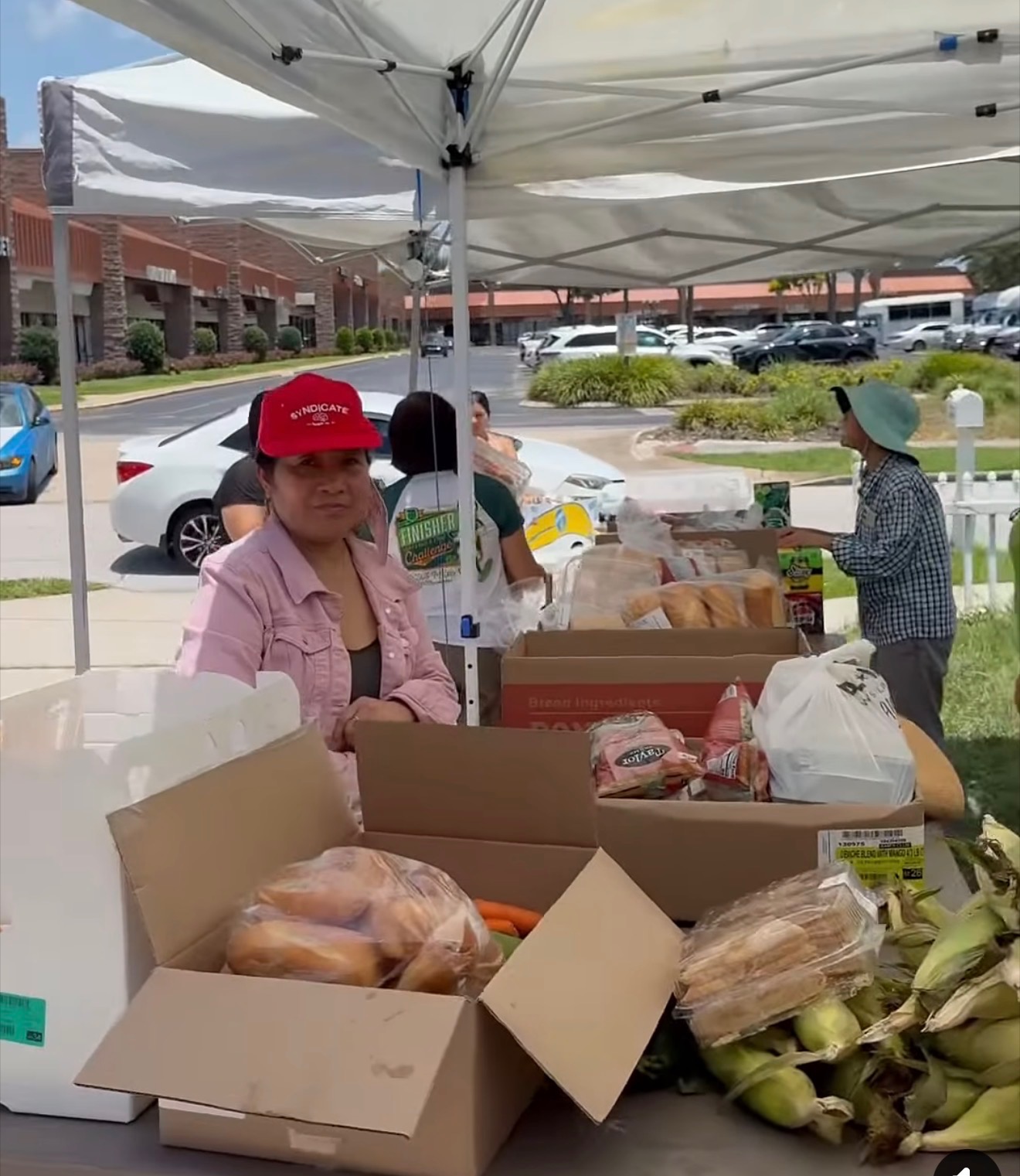 A cheerful coordinator seated behind a table stacked with produce and pantry staples